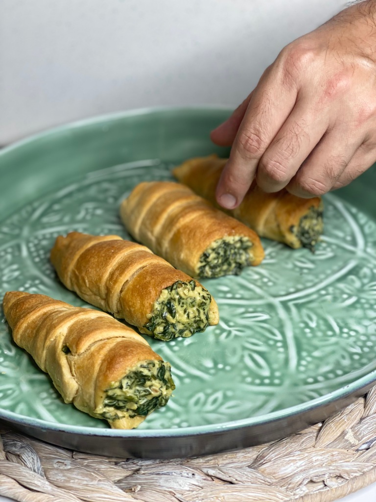 A man's hand picking up a vegan creamed spinach stuffed pastry roll.